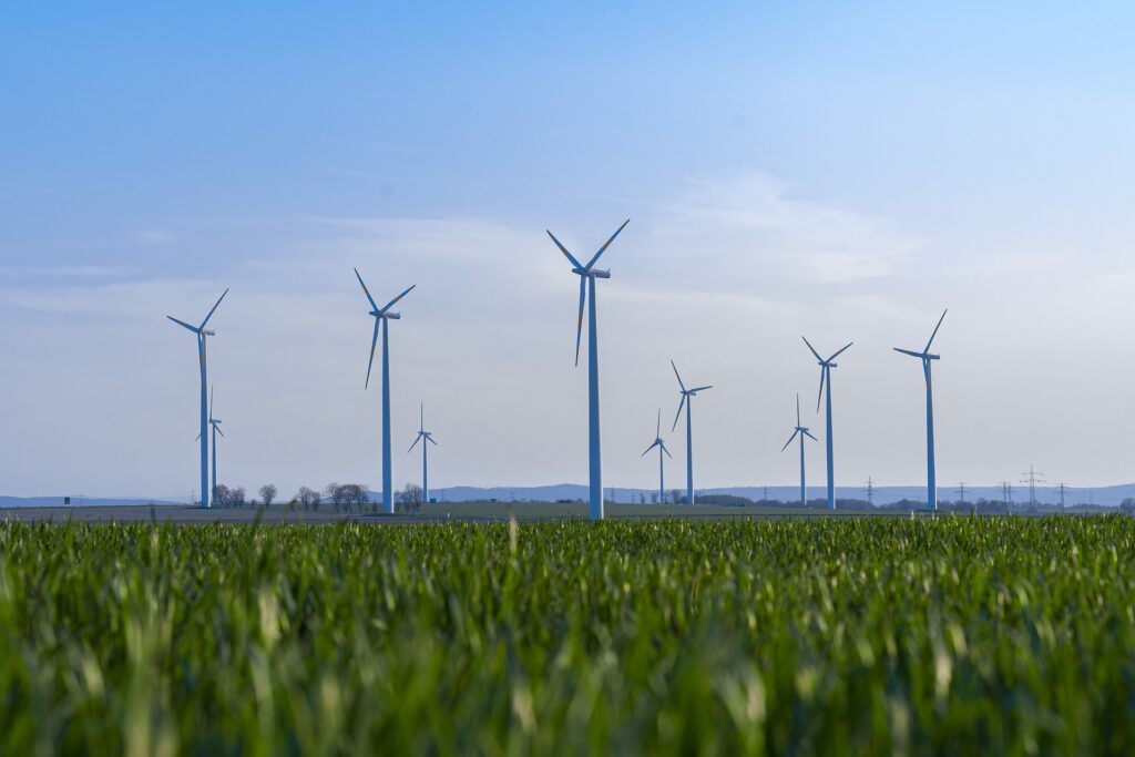 Investimentos sustentáveis: geradores de energia eólica em frente a céu azul e sobre grama verde.